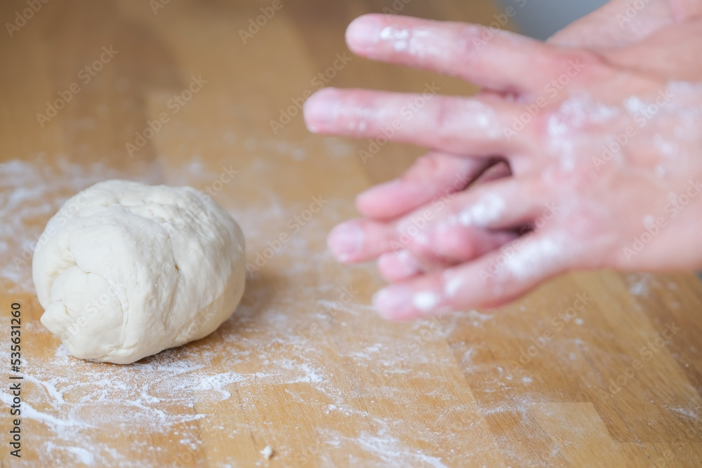 Kneading dough on the wooden table, lump of dough next to a hands in flour Kneading dough on the wooden table, lump of dough next to a hands in flour