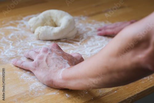 Close up of hands in flour lean on the table next to dough 