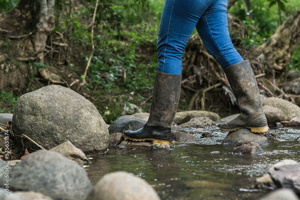 migrant woman crossing a stream wearing blue jeans and black marsh boots. hiking through the dense colombian forest. wet boots. hiking concept. migrant woman crossing a stream wearing blue jeans and black marsh boots. hiking through the dense colombian forest. wet boots. hiking concept.