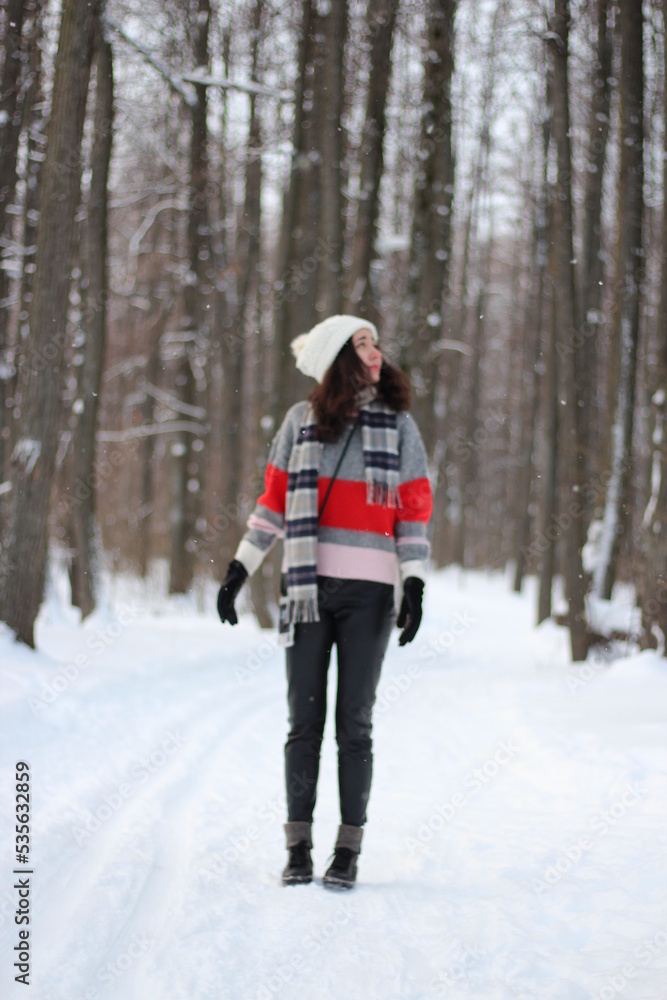 A young woman in a sweater and a white hat in the forest. Full length portrait. Snowing. Winter atmosphere. Walk in the forest.