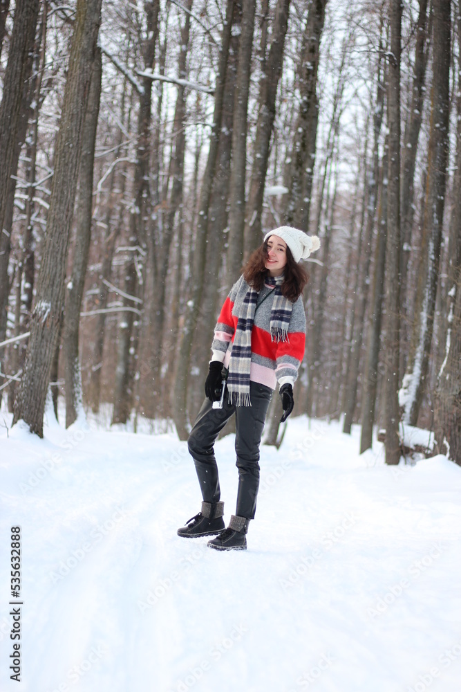 A young woman in a sweater and a white hat in the forest. Full length portrait. Snowing. Winter atmosphere. Walk in the forest.