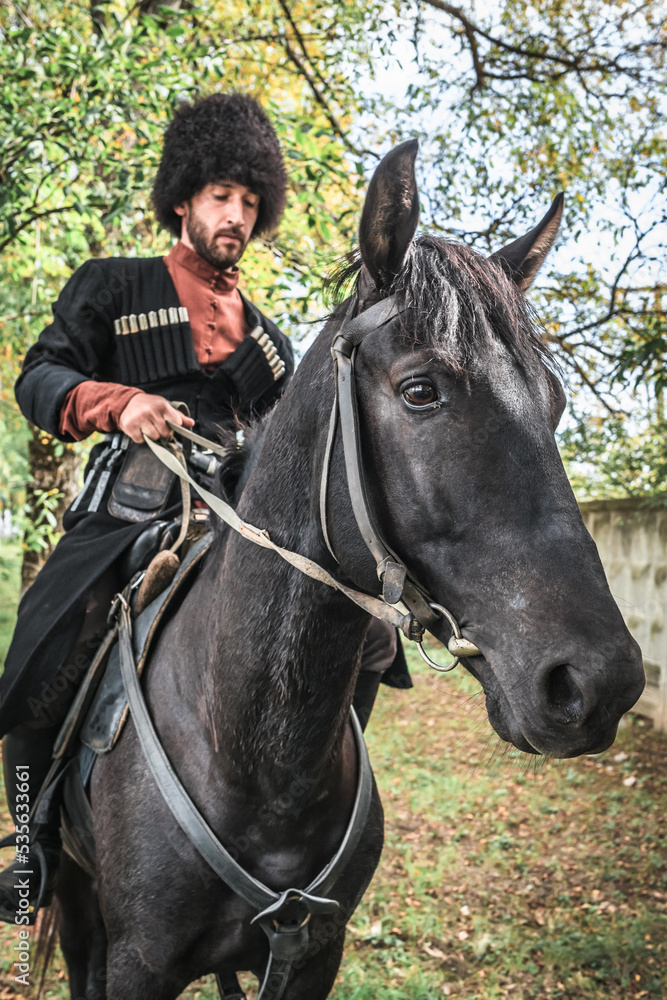 A man with a beard Circassian highlander Caucasian national costume takes care of a horse A man with a beard Circassian highlander Caucasian national costume takes care of a horse