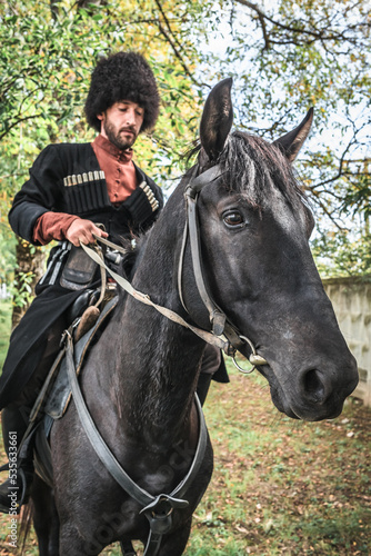 A man with a beard Circassian highlander Caucasian national costume takes care of a horse