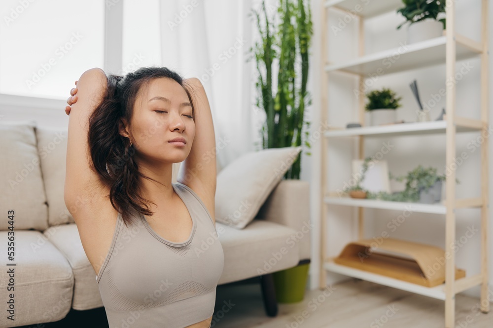 Young Asian woman her laptop doing sports and yoga repeating exercises on the video at home in the lotus position stretching the muscles of the back and arms, home workouts for the body lifestyle