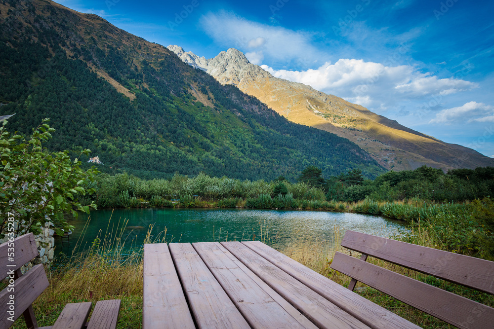Table with benches against the backdrop of a mountain landscape and a lake. North Ossetia Table with benches against the backdrop of a mountain landscape and a lake. North Ossetia