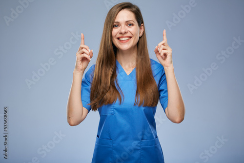 Smiling nurse woman pointing fingers up. Isolated female portrait.
