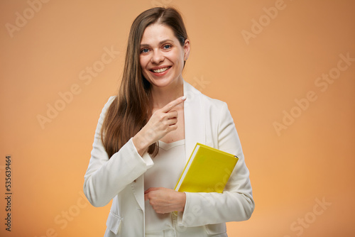 Teacher woman with yellow book in white suit pointing at side, isolated female portrait.