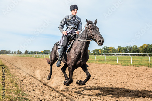 Cossack man in a national costume is galloping rapidly on a black horse around the hippodrome