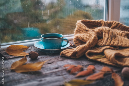 Cup of coffee on a wooden autumn background. Tea and autumn leaves near the window. Coffe on the background of a window with rain.