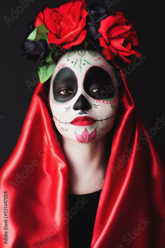 attractive woman with sugar skull make-up, red dress, flowers on her head, posing with confidence and expressive look