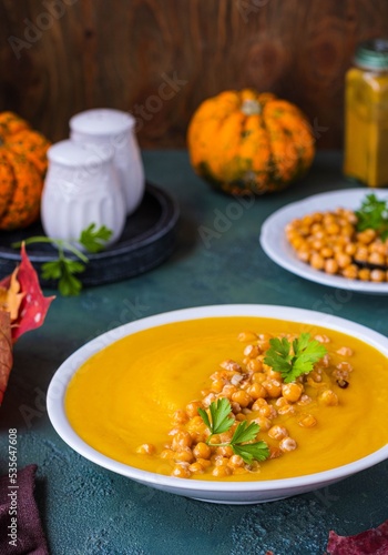 Creamy pumpkin soup with fried chickpeas garnish in a white ceramic plate on a green concrete background. Thanksgiving Day