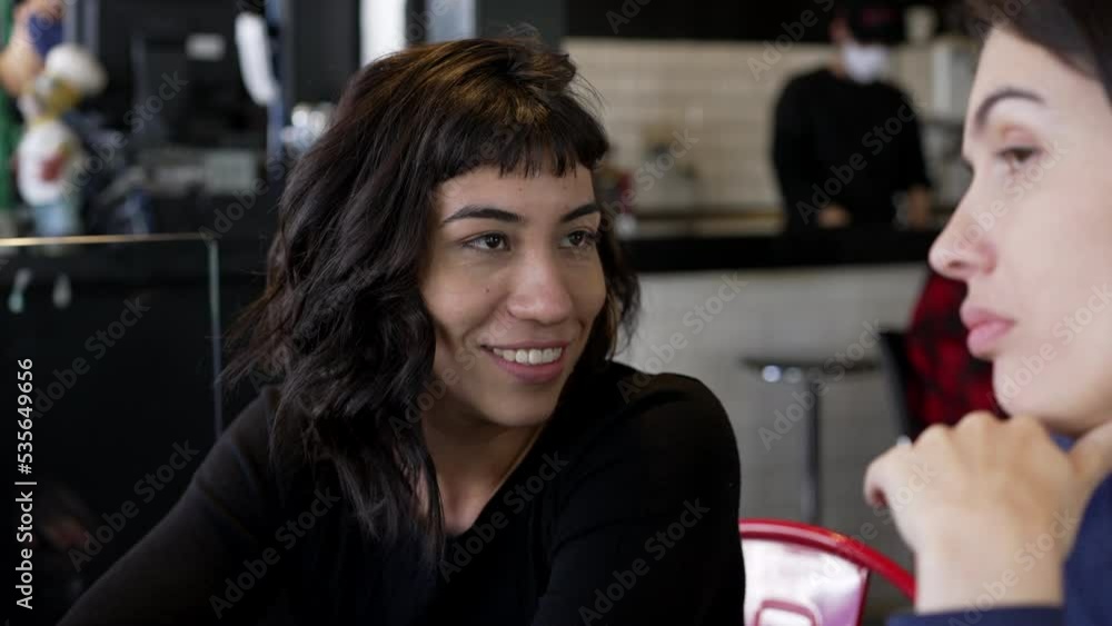 Two female friends in conversation at restaurant. Casual candid friendship sharing gossip Two female friends in conversation at restaurant. Casual candid friendship sharing gossip