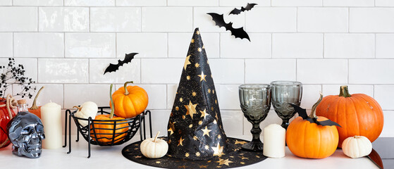 Halloween banner design with witch hat, pumpkins, halloween decorations on white table. Halloween home interior design.