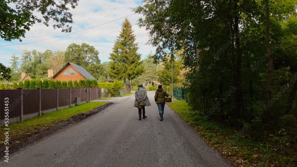 Backside view: Two older women going to harvest mushrooms in a foorest holding wooden baskets real time Backside view: Two older women going to harvest mushrooms in a foorest holding wooden baskets real time