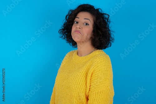 Fotografia young beautiful woman with curly short hair wearing yellow sweater with snobbish expression curving lips and raising eyebrows, looking with doubtful and skeptical expression, suspect and doubt