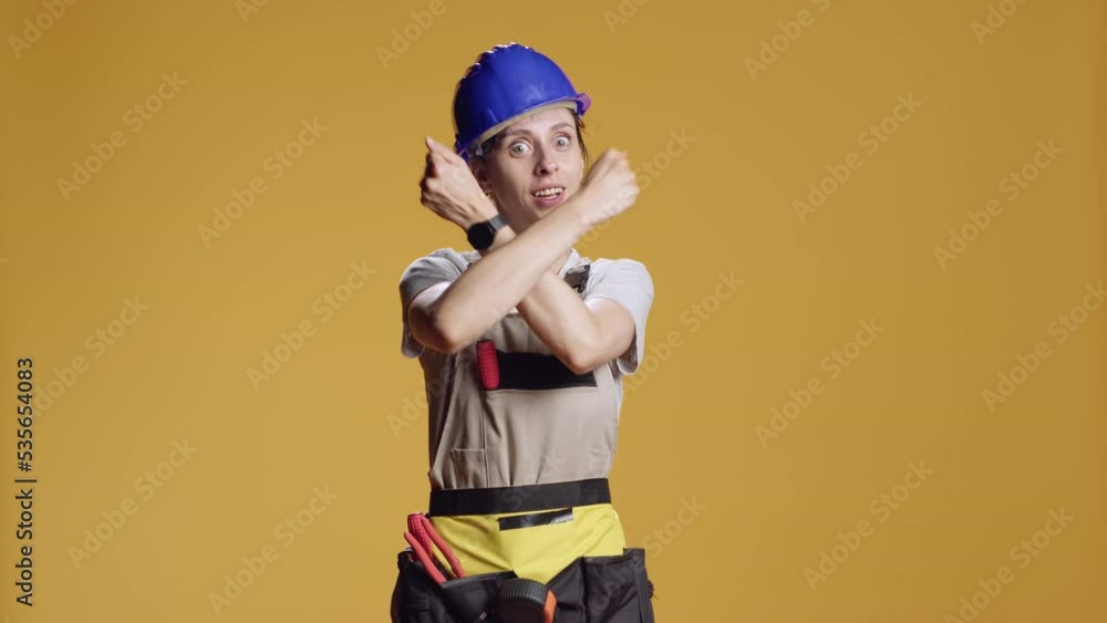 Portrait of strong handywoman doing x shape sign with arms crossed, advertising stop and break gesture over yellow background. Constructor showing timeout and finish symbol in studio. Portrait of strong handywoman doing x shape sign with arms crossed, advertising stop and break gesture over yellow background. Constructor showing timeout and finish symbol in studio.