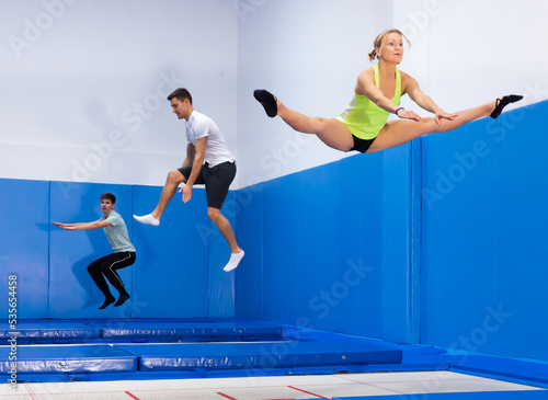 Smiling female and males jumping and bouncing on a trampoline during workout in modern fitness center