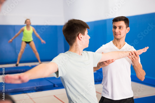 Skilled coach holding training with teenager in trampoline room, explaining basic jumping tricks..