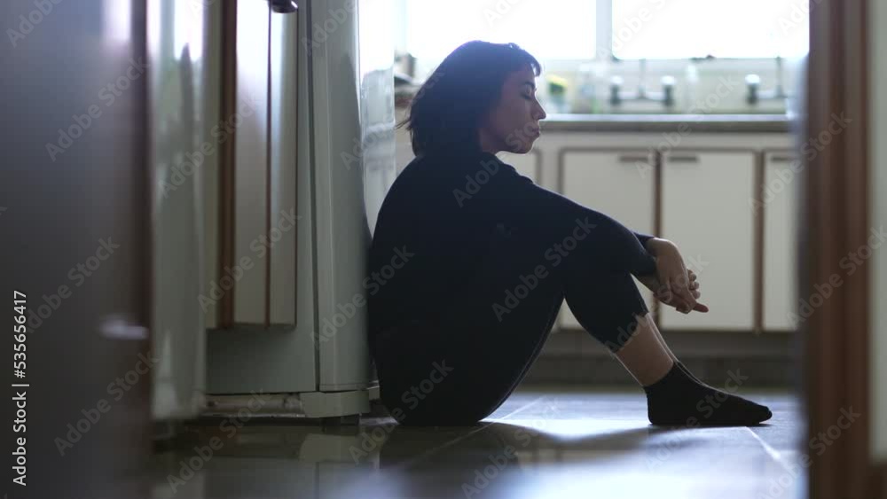 Woman suffering from depression sitting on floor at home having emotional angst and pain. Sad unhappy person suffering from mental illness Woman suffering from depression sitting on floor at home having emotional angst and pain. Sad unhappy person suffering from mental illness