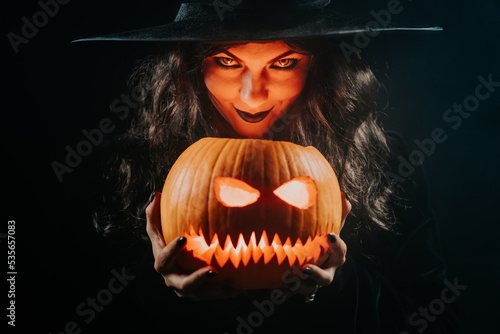 Foto Mysterious black witch with pumpkin as head of jack-o-lantern on dark backdrop