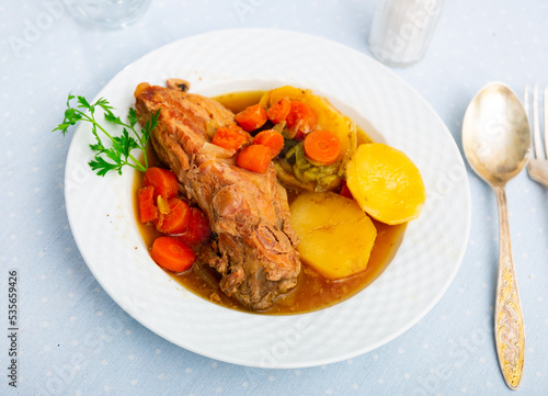 Delicious dish of stewed pork ribs with potatoes and vegetables, decorated with a fresh sprig of greenery