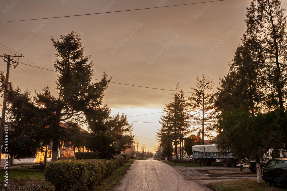 Typical countryside road in the village of Banatsko novo selo, a serbian village of the Banat region of Vojvodina, Serbia, at dusk with an old rusted trucks parked, waiting to plough fields.....