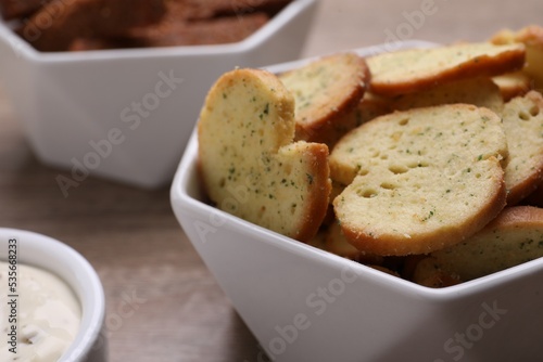 Crispy rusks in bowl on wooden table, closeup