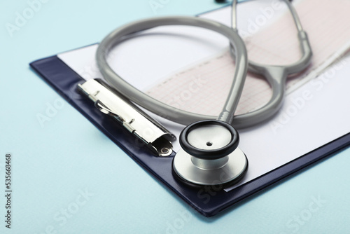 Clipboard with stethoscope and cardiogram on turquoise background, closeup