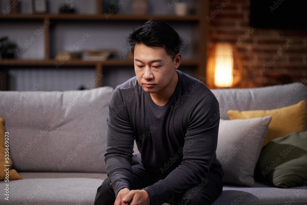 Depressed Asian man is sitting on the couch. Stress, fatigue, burnout, apathy. Depressed Asian man is sitting on the couch. Stress, fatigue, burnout, apathy.