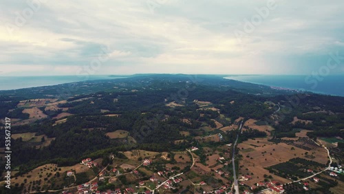 Breathtaking drone aerial view of Paliouri Kassandra in Greece. Connection between traditional human-built town and wooded hills of pine forest. Cloudy sky. High quality 4k footage photo