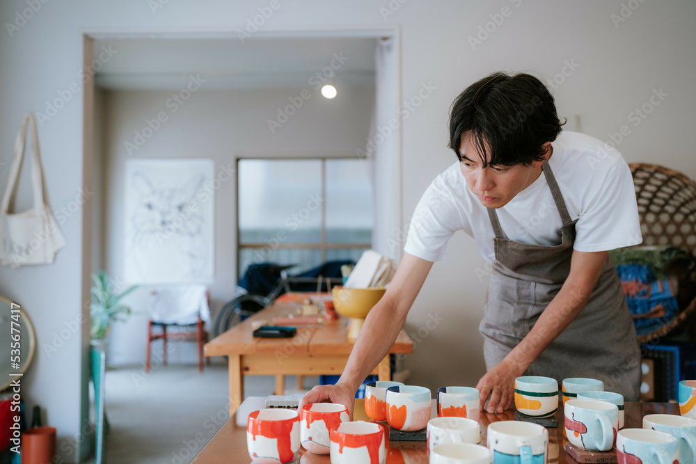ギャラリーでマグカップを並べる男性店員 ギャラリーでマグカップを並べる男性店員