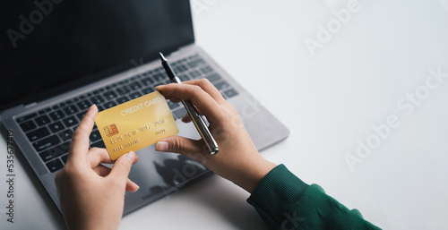 Close-up of women hand holding credit card while online paying on laptop, focus on the hand and on the card, purchases and Internet concept.