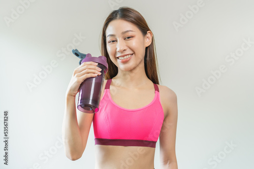 Diet meal replacement for weight loss, smile asian young woman standing in sportswear, holding protein shake for drink, having sports supplement for muscle after workout, isolated on white background.