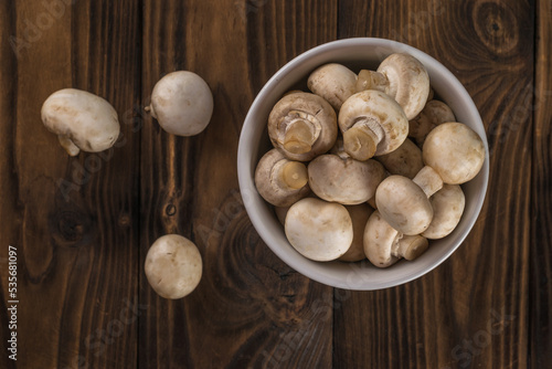 A bowl with champignons and three separate mushrooms on a wooden background.