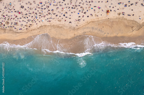 imagen cenital desde dron de una playa color turquesa con mucha gente disfrutando de las olas y la arena