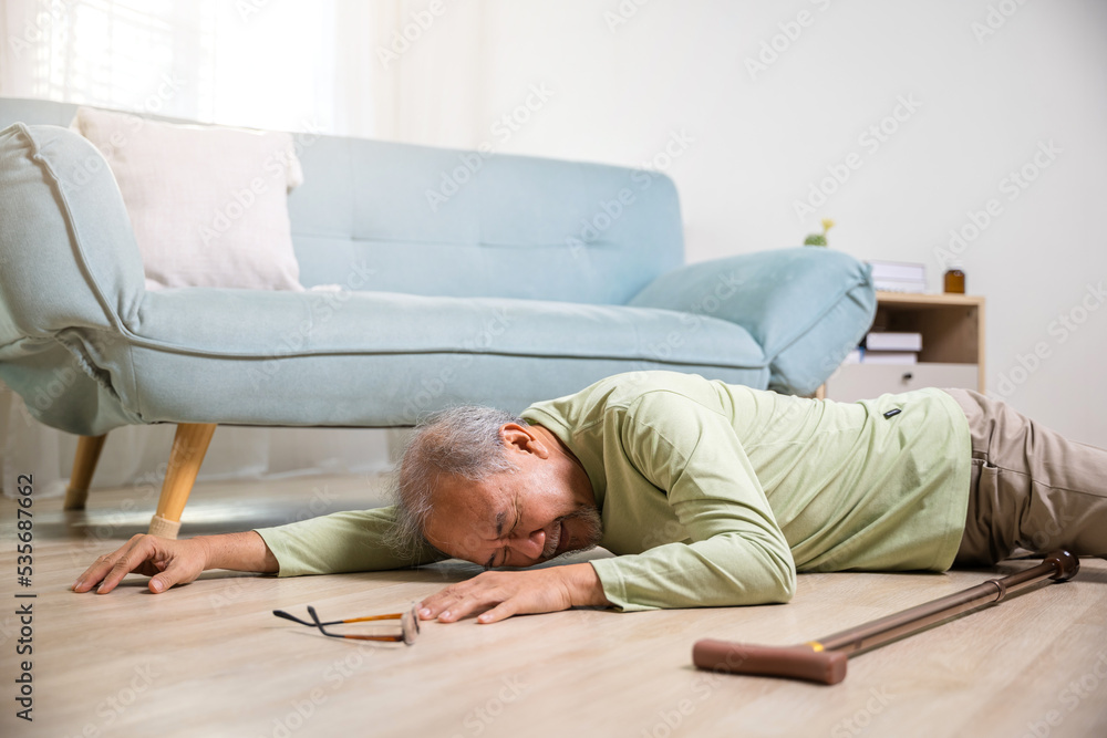 Sick senior man beside couch on rug in living room at home, Elderly mature grandfather having an accident after doing physical therapy alone with walking stick, Health care and medicine concept