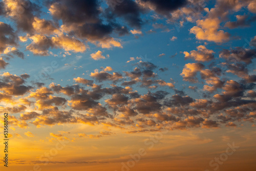 bright summer blue sky with white fluffy clouds of various shapes and sizes, cirrus, heap clouds, golden from sunlight.