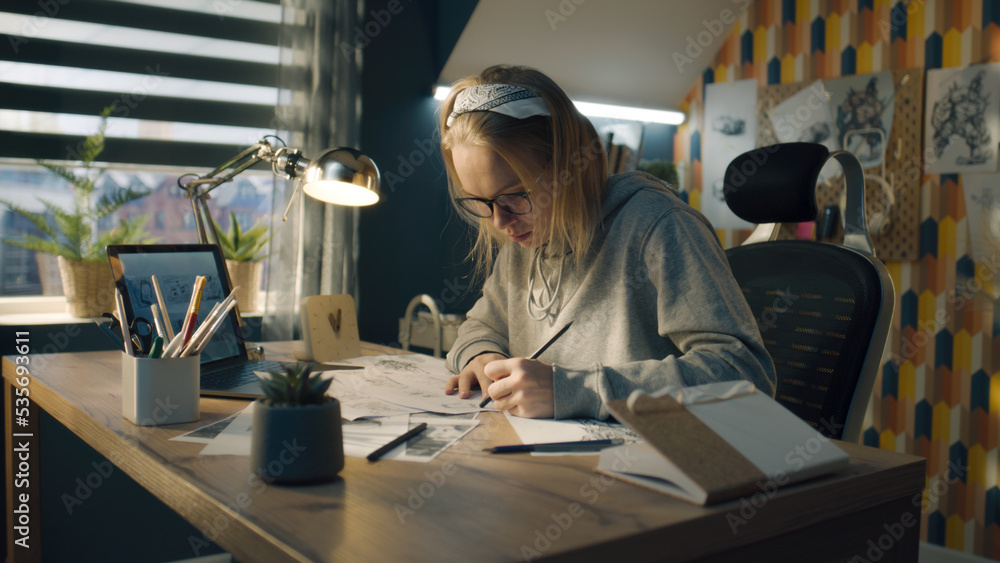 A blonde woman working on a storyboard in a home based design studio. Focused woman dressed in a hoodie drawing pencil sketches. Making storyboard as a roadmap for the video.