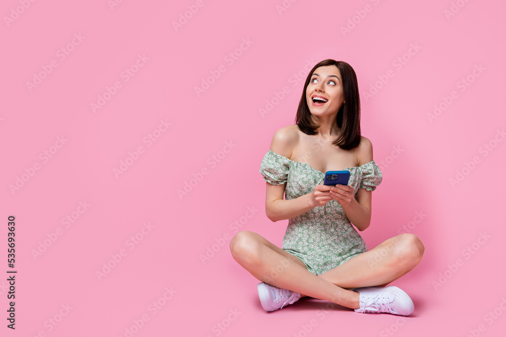 Full size photo of sweet lady sit hold telephone look up wear dress boots isolated on pink color background Full size photo of sweet lady sit hold telephone look up wear dress boots isolated on pink color background