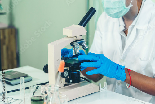 Indian Scientist man look into Microscope research in science laboratory. Asian biochemistry scientist using microscope in laboratory chemistry labs. Covid-19 medical research scientific experiment
