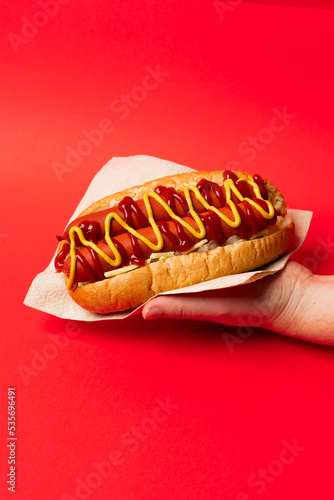 American Hotdog held in hand in a napkin against a red background