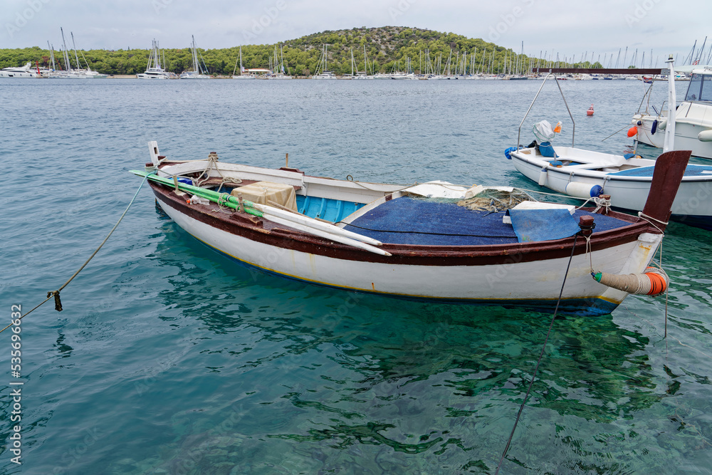Fishing boat, white fishing boat for rowing in the beautiful blue crystal clear waters of the Croatian Mediterranean. In the background there is a marina and green mountains.