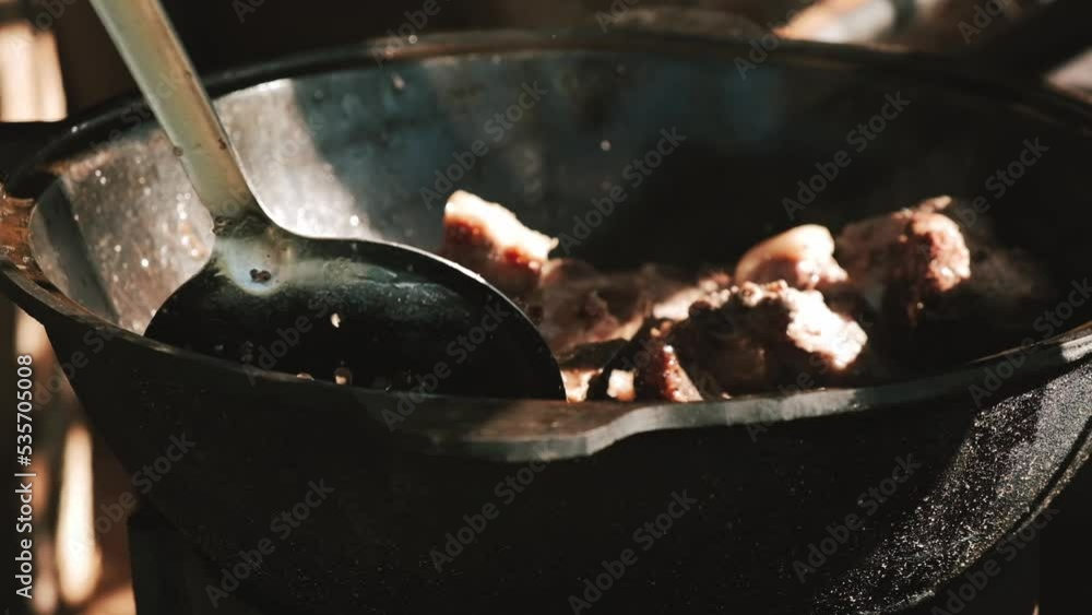 A man roasts meat in a cauldron on an open fire.Close up,slow motion. A man roasts meat in a cauldron on an open fire.Close up,slow motion.