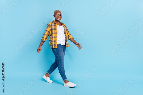 Full length photo of pretty cute woman dressed plaid shirt walking empty space isolated blue color background