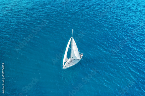 Aerial view of beautiful white sailboat sailing in the blue sea on a sunny day. Peaceful landscape with yacht. Top view of boat