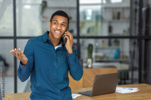 Portrait of successful young african american business man talking using a mobile phone standing in modern office