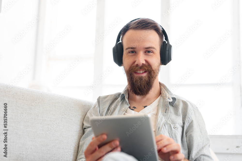 Handsome bearded man using digital tablet while resting on couch at home Handsome bearded man using digital tablet while resting on couch at home