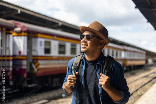 Freedom traveler young asian man at terminal train station. Happy tourist travel by train on vacation time holiday weekend trip. Male Backpacker arrival at platform railway.
