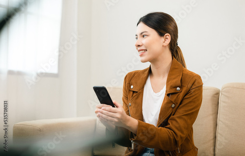 Beautiful young women using mobile phone sitting on sofa in living room. Using smartphone. Woman Shopping online store. Relax time at home