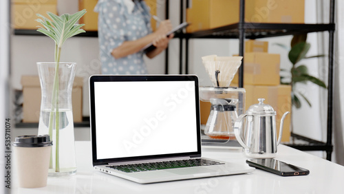 Blank screen mock up laptop computer, Young woman working in the background. © RedcupStudio